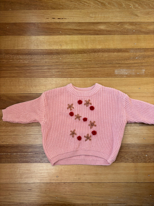 Pink sweater with embroidered designs on a wooden surface