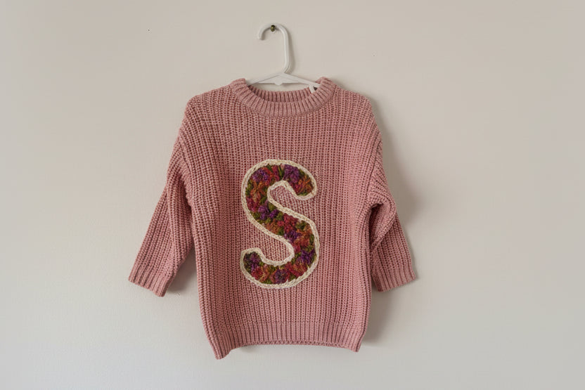 Pink knitted sweater with a colorful letter